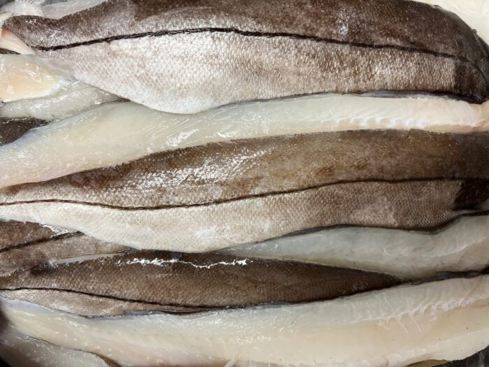 Fresh haddock fillets layered in a row showing both silver skin and white flesh.