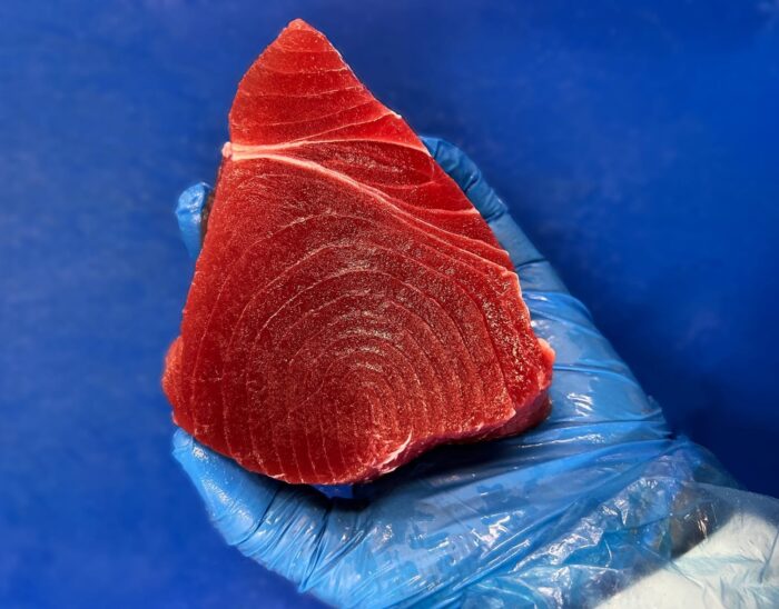 A hand in a blue protective glove holding a tuna steak above a blue chopping board