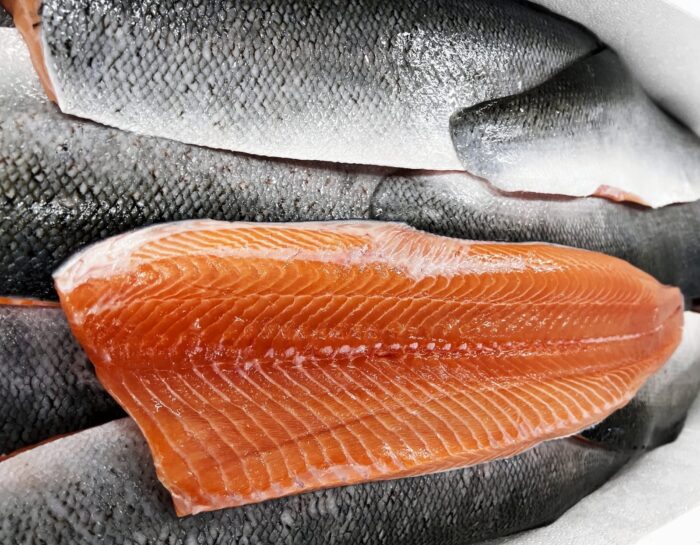 A fresh salmon fillet flesh side up on top of a neat bed of skin side up salmon fillets.